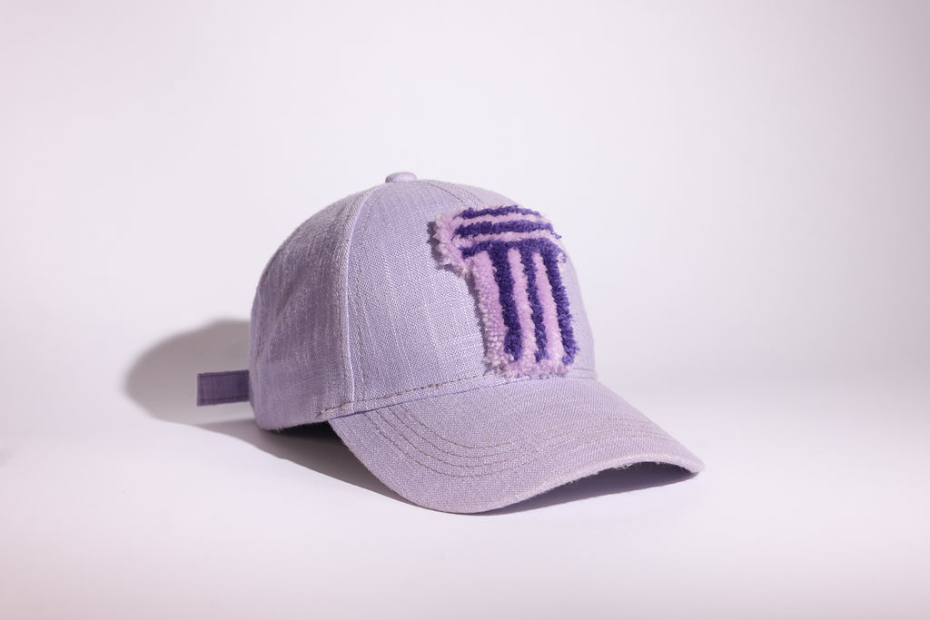 A light lavender baseball cap with a textured, embroidered purple TUFTED logo on the front, photographed on a clean white studio background.