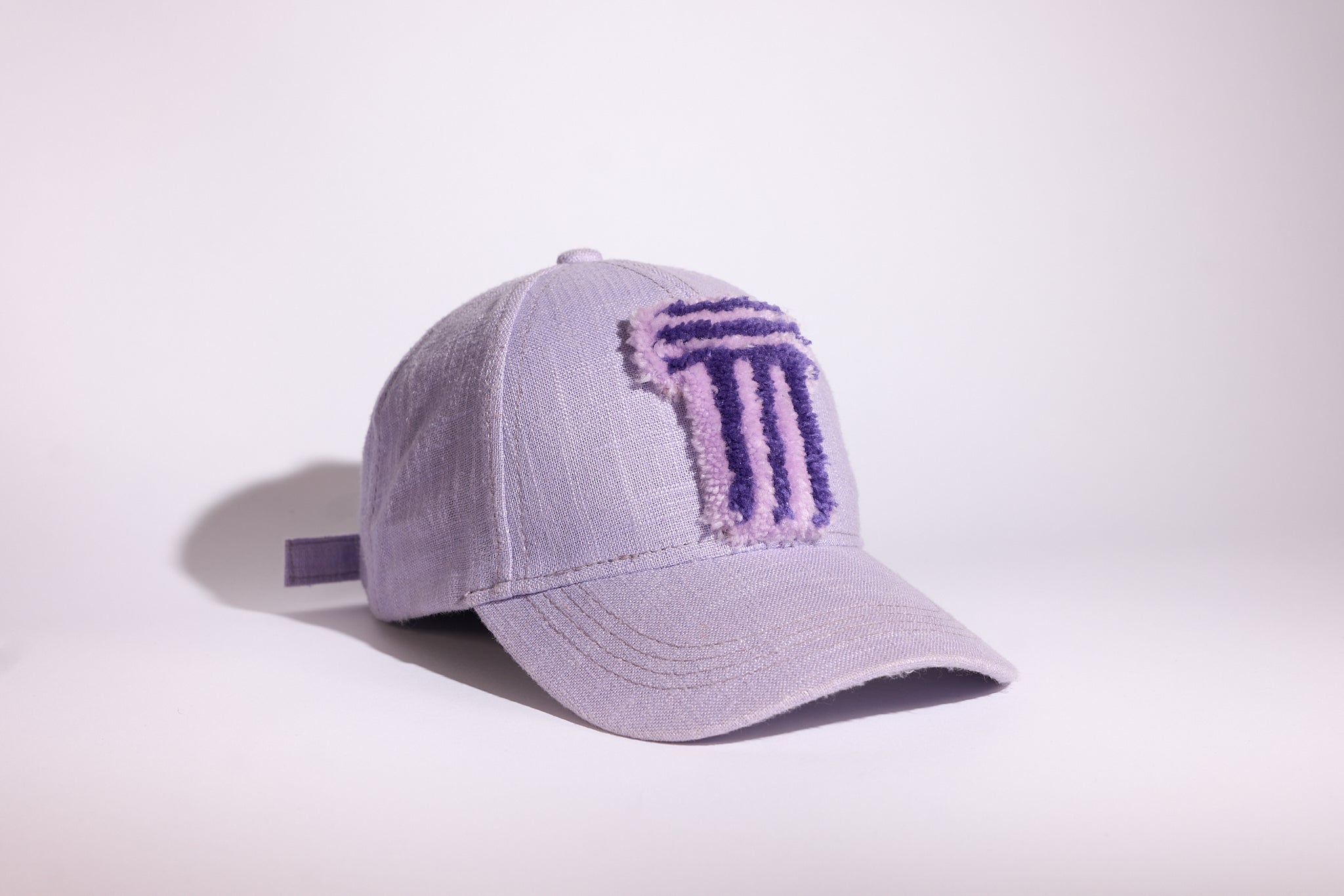 A light lavender baseball cap with a textured, embroidered purple TUFTED logo on the front, photographed on a clean white studio background.
