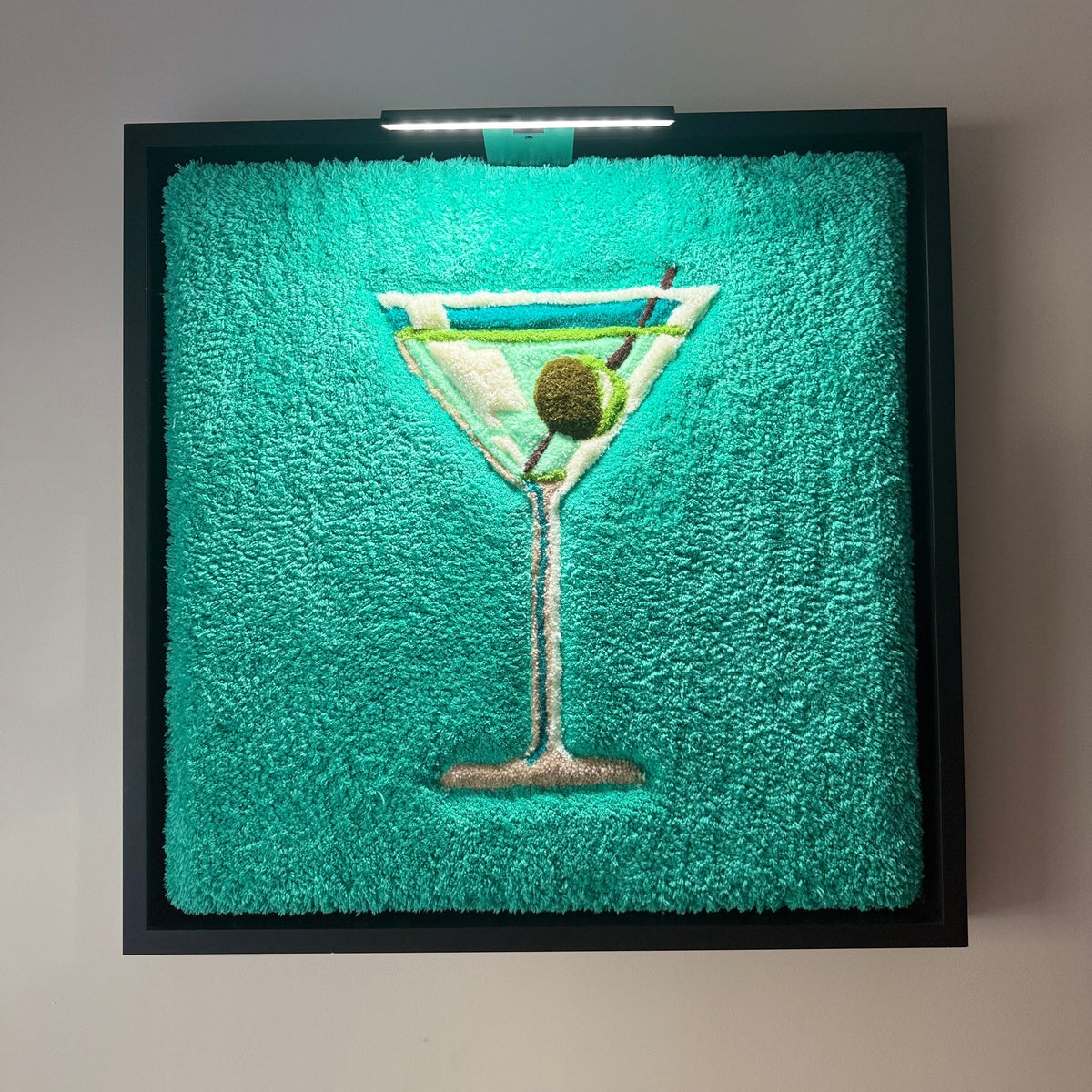 VESPER, œuvre tuftée contemporaine de Ninon Dechavanne représentant un verre à cocktail sur fond turquoise, encadrée dans une caisse américaine noire.